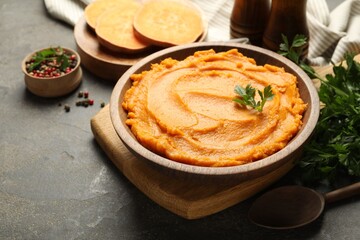 Delicious mashed sweet potatoes in bowl, pieces of fresh vegetable, spices and spoon on gray textured table, closeup