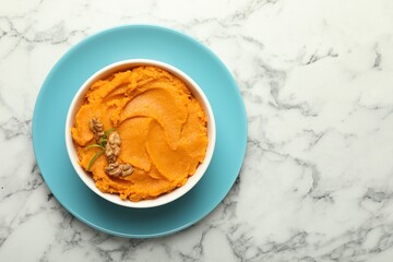 Delicious mashed sweet potatoes with walnuts in bowl on white marble table, top view. Space for text