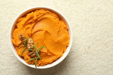 Delicious mashed sweet potatoes with walnuts and rosemary in bowl on light table, top view. Space for text