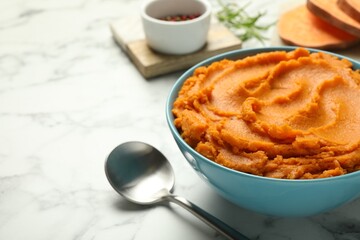 Tasty mashed sweet potato in bowl and spoon on white marble table, closeup. Space for text