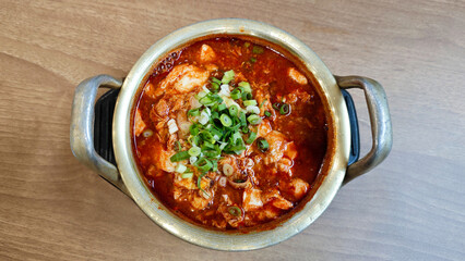 Close-up of Sundubu Jjigae Korean Soft Tofu Stew with Green Onion Garnish in a Traditional Brass Pot on a Wooden Table