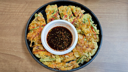Close-up of Korean Haemul Pajeon Seafood Pancake with Soy Dipping Sauce on Black Plate on Wooden Table