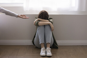 Girl crying seated on floor, mother hand extended to her like symbol of support, help, solace in...