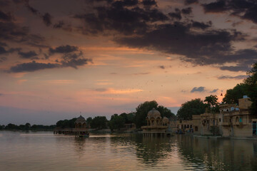 Naklejka premium Beautiful sunset at Gadisar lake, Jaisalmer, Rajasthan, India. Setting sun and colorful clouds in the sky with view of the Gadisar lake. Connected with Indira Gandhi Canal for continuous water supply.