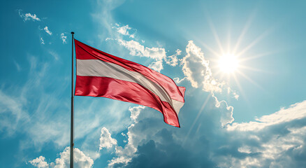 The flag of Austria flutters in the wind on a flagpole against a sky with clouds on a sunny day.