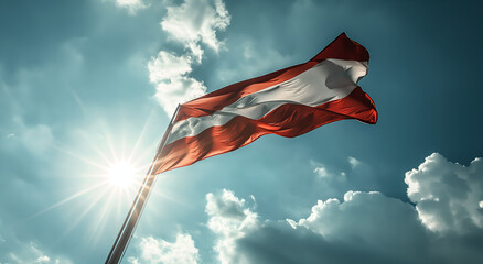 The flag of Austria flutters in the wind on a flagpole against a sky with clouds on a sunny day.