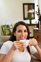 Chica bonita sonriendo a la cámara mientras toma una deliciosa taza de café caliente por la mañana. Toma vertical.