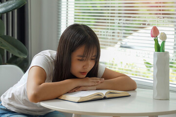 Young Asian woman slumped over the table, chin on her hands, reading a book While she was sitting...