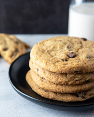 Chocolate Chip Cookies Stacked on a Plate Next to Broken Cookie and Glass of Milk