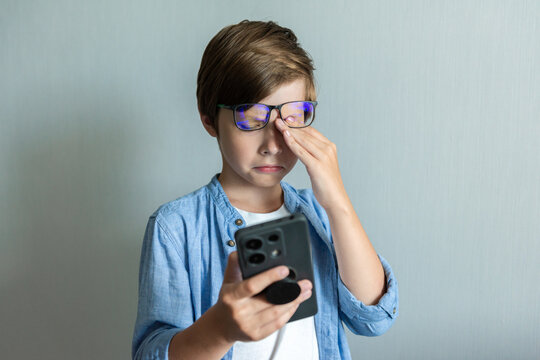 Child boy rubs his eyes for looking at phone. Hyperopia myopia astigmatism glaucoma and addiction to gadgets