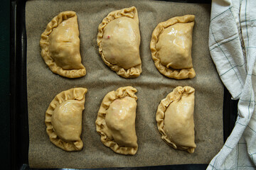 Step by step process of preparing homemade empanadas with meat, vegetables and quail egg. Six empanadas on the tray before baking.