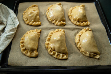 Step by step process of preparing homemade empanadas with meat, vegetables and quail egg. Six empanadas on the tray before baking.