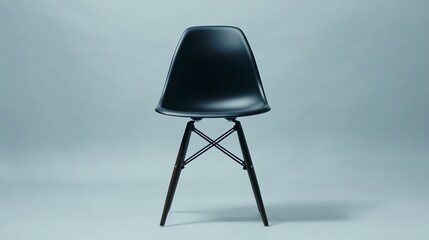A contemporary dining chair with a molded plastic seat in matte black and thin, tapered wooden legs, centered on a plain, light gray background