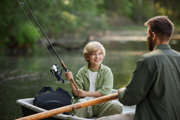 Child and adult enjoying peaceful fishing session on calm lake from small boat while child holding fishing rod having conversation in relaxed setting