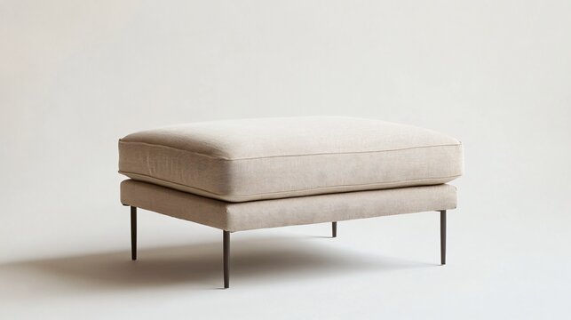 A stylish modern ottoman with a rectangular design, upholstered in soft, beige fabric, and featuring thin metal legs, centered on a neutral background