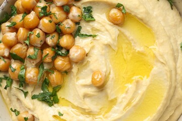 Delicious hummus with olive oil, chickpeas and parsley in bowl, top view