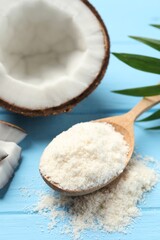Fresh coconut flour in spoon, nut and palm leaf on light blue wooden table