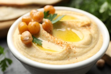 Delicious hummus with olive oil, chickpeas and parsley in bowl on grey table, closeup