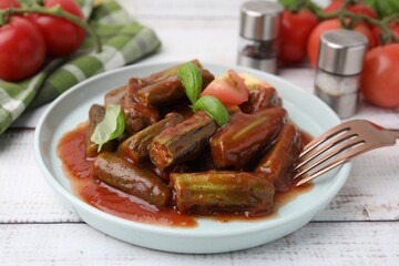 Tasty stew with okra, tomato sauce and basil on white wooden table, closeup