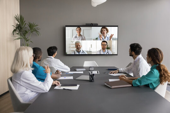 Virtual meeting event of diverse medical internists professionals, communicate remotely using videoconference application, gathered together in boardroom of clinic. Opinion, exchange, decision-making