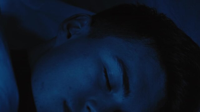 Night terror. Bad dream. Anxiety stress. Disturbed scared guy woke up opened eyes in bed late at home in dark blue light.