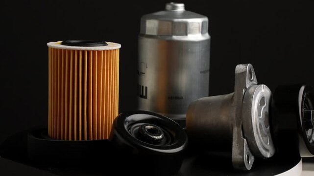 Slowly rotating auto parts on black background. Fuel, oil filters and tension roller with poly V-belt are rotating around. Auto parts replacement concept.