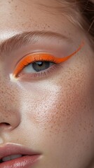 Obraz premium Bright orange eyeliner accentuates the eye of a young woman with freckles and luminous skin