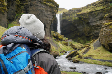 Hiker man arriving at a landscape with impressive waterfall in Iceland. back view. dressed in the mountain suit and hat