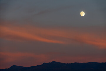 Obraz premium Full moon between orange clouds at dusk