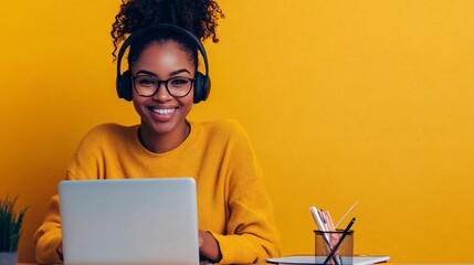 A customer service representative wearing a headset, smiling while sitting at a desk with a laptop and notepad, light solid color background