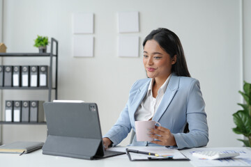 Businesswoman working from her office, using a tablet and enjoying a cup of coffee