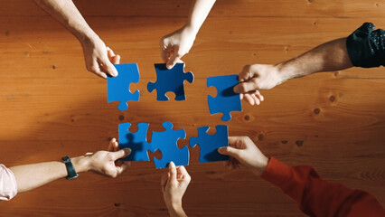 Top down view of skilled business people separated blue jigsaw puzzle on meeting table. Group of...