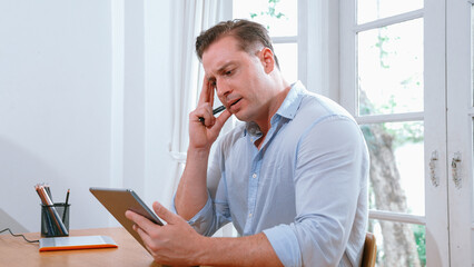 Businessman struggle to solve work problem from home using laptop, sitting on his desk at home office with stressed and frustrated expression, trying to figure out solution for problem. Synchronos