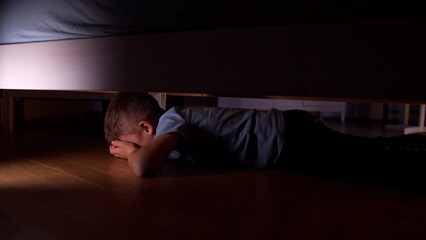 Scared child hiding under the bed at night