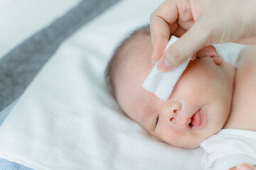 Mother cleans newborn's eyes with cotton and saline solution.