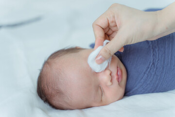 Mother cleans newborn's eyes with cotton and saline solution.