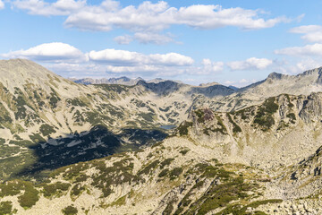 Panoramic view of mountain range and glacial lake in between the peaks with a blue sky and flufy white clouds.