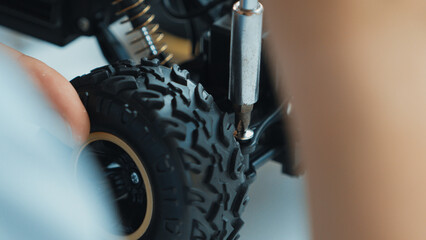 Fototapeta premium Close up of young student hand tighten the nut at car model wheel by using screwdriver. Caucasian teenager repairing or fixing robotic machine while inspect construction. Focus on hand. Edification.