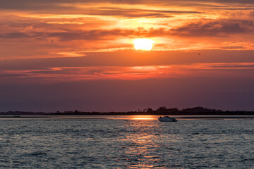 Obraz premium Fiery Sunset on the Sea with Distant Boat, View from Grado Lighthouse, Italy: Red Orange Colors in the Sky.