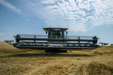 Front view of a combine harvester working in a wheat field under a bright sky. High-efficiency...