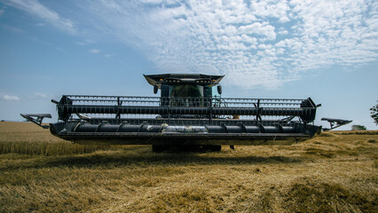 Front view of a combine harvester working in a wheat field under a bright sky. High-efficiency...