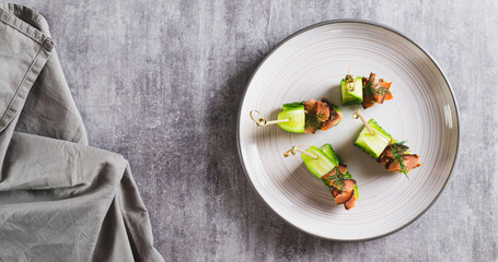 Delicious canapes of cucumber, red fish and dill on a plate on the table top view web banner