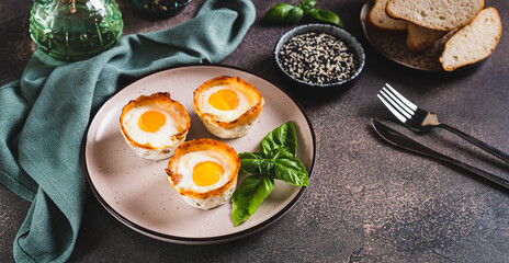 Chicken eggs baked in bacon and basil leaves on a plate on the table web banner