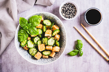 Fresh cucumber and fried tofu salad with basil leaves in bowl on table top view