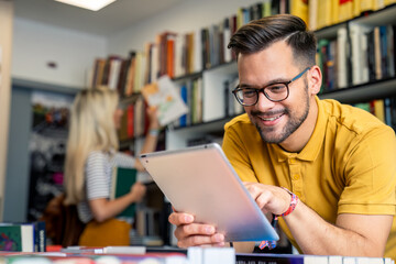 A cheerful Caucasian male student browses information on his digital tablet while a female student...