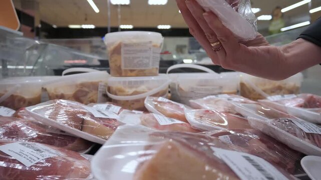 Close-up shopper choosing package fresh meat in store.