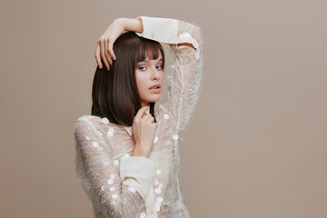 Beautiful young woman with short brown hair posing confidently against a neutral beige background,...