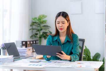 Focused and Determined: A professional woman in a teal blouse meticulously analyzes data on a tablet, showcasing dedication and focus in a modern office setting. The image conveys a sense of concentra
