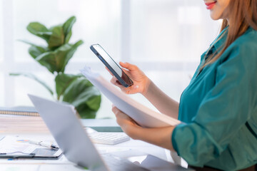 Mobile Office Efficiency: Businesswoman streamlining workflow, reviewing documents with smartphone integration at her desk.