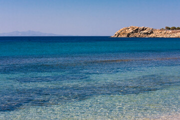 A breathtaking Mediterranean landscape in Greece features turquoise sea water meeting the sandy shore of a Crete island bay under a clear blue summer sky
